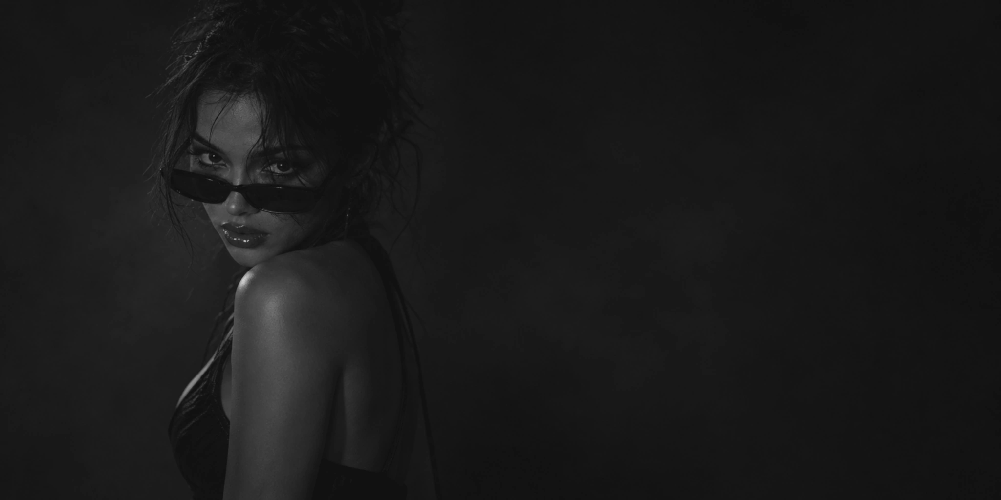 Dark monochrome portrait of Maxine Meyer looking over sunglasses, with open shadowed space beside her